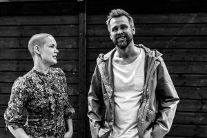 En svartvit bild av Johannes och Sara. Sara kollar på Johannes och säger någonting, Johannes tittar in i kameran och ler stort.