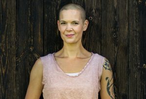 Närbild av Sara, i ett rosa linne framför en mörkgrå trävägg.