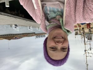 Sara i mössa och rosa jacka vid en kaj vid havet.