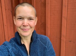 Sara i blå tröja mot en faluröd trävägg.