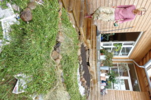 En träfärgad byggnad meden liten kulle nedanför täckt med gräsklipp.