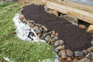 En liten bädd med svart jord och i bakgrunden ett träfärgat däck.