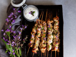 Gyllengrillade kycklingspett bredvid örter som blommar i lila.
