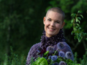 Porträttbild av Sara i lila kofta och en bukett blå blommor i famnen.