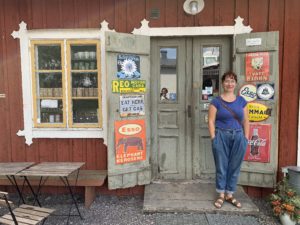 En kvinna i blått står framför en gammal lanthandel.