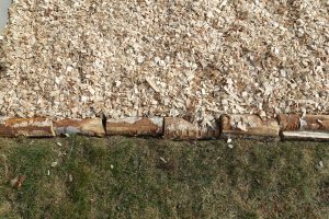 En bild på en kant av vedträn mot träflis och gräs.