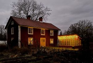Ett rött hus och ett växthus framför med ljusslingor.