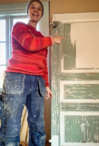 Sara står i arbetskläder bredvid en dörr som skrapas.