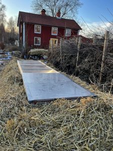 Närbild på varmbänken med rött hus i bakgrunden.