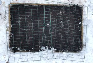 En pallkrage i snö fotograferad ovanifrån, med grönt galler på toppen.