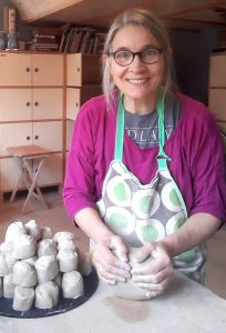 Kvinna står med lerklumpar och knådar.