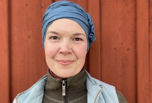 Porträtt på Sara i blå mössa mot röd vägg.