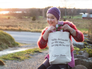 Sara sitter på stenmuren med tygåsen och fröer i handen.